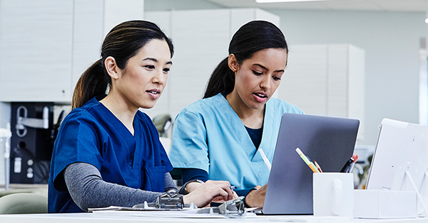 two healthcare professionals work on a laptop together